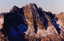 A reddish-brown mountain range. The tops are ragged and sharp and there is dirty old snow on some of the lower parts of the mountains.