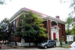 A two-story formal brick building surrounded by trees