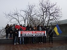 twenty masked activists posing with a Ukrainian flag and a Right Sector banner showing trident as ship anchor at a Euromaidan event in Odesa