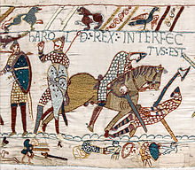 Tapestry depicting a scene from a battle. From left to right: soldier with shield, soldier with shield and weapon, and a rider on a horse, trampling another soldier armed with an axe. The inscription at the top reads HAROLD REX, signifying that one of the figures is a representation of King Harold Godwinson.