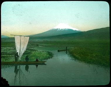 People in boats on waterways through rice fields; snow-covered mountain in background