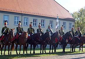 Photo of eight horsemen dressed in Austrian hussar uniforms of the early 1800s, with red shako, dark green jackets, and red breeches