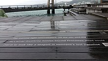words in metal on a wooden boardwalk with the harbour in the distance