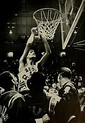 A basketball player cutting a net away from the rim.