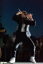 Lorde performing onstage with spontaneous and unchoreographed moves, wearing a blazer and white sneakers