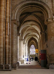 A side aisle with masonry of massive proportions is ribbed with arches of a bold profile.