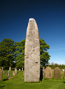 a cemetery over which towers a large standing stone with some sort of cap