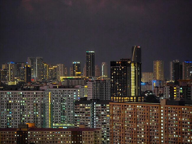 A panoramic view of the cityscape, dominated by skyscrapers and apartment blocks, at dusk.