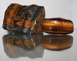 A polished reddish brown stone which is bisected by a band containing golden fibers