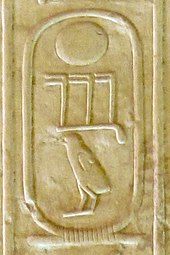 Three hieroglyphs inscribed on a cream-colored stone: a circle, beneath it three toes and a chick