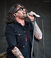 a bearded man with long brown hair and sunglasses singing into a microphone