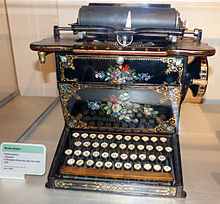 An ornately decorated typewriter with black lacquer, gold detailing and various floral arrangements