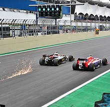 A picture a Lotus E23 Hybrid and a Marussia MR03B driving side by side during the 2015 Brazilian Grand Prix, with sparks flying up from behind the Lotus.