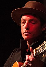 A close-up of a man with a hat and guitar
