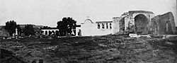An overall view of the "Mission of the Swallow" around the time of St. John O'Sullivan's arrival in 1910. The Mission's once-renowned California pepper tree can be seen just to the left of the adobe church's espadaña.