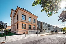 Bild des Hauptgebäudes der Hochschule Zittau-Görlitz in Zittau, charakterisiert durch seine historische Architektur, mit hervorgehobenen Fenstern und einer deutlichen Eingangstür. Die Umgebung zeigt gepflegte Grünflächen und einen klaren Himmel, was den akademischen Charakter des Ortes unterstreicht.