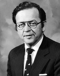 Senator Ted Stevens in 1979, wearing a black suit & dark tie. The image is in black & white. Wikipedia caption reads "Ted Stevens was key in the bill's passage.".