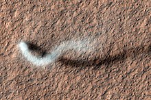 A towering dust devil on the Martian surface casts a serpentine shadow, illustrating Mars' unique weather conditions.