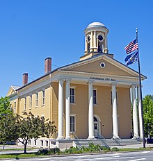 A pale-yellow two-story building, seen from the side, with a classically styled colonnade on the front underneath a small domed cupola