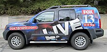 A KSTU news van, with Fox 13 logo and fox13now.com URL emblazoned on it, parked outside a building