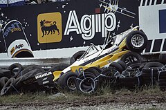 A badly damaged yellow-and-white racing car after impact into a tyre wall