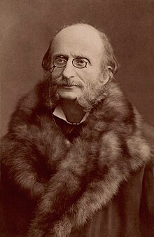 photograph of ageing white man, balding, with moustache and side whiskers, in a huge fur coat and wearing pince-nez