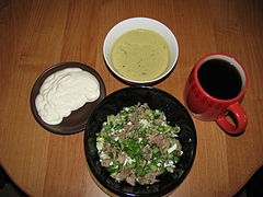 Classic okroshka with beef. Nearby are plates of smetana, a special dressing (made from pounding yolks, Russian mustard, horse radish, green onion, and salt), and a cup of kvass.