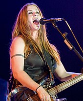 A woman in a black vest singing and playing an electric guitar.