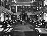 A black-and-white photograph of a parliament in session, with MLAs sitting in their places