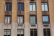 View of some windows on the third to fifth stories. There are notches at the tops of each cast stone pier. Above are vertical brick piers, as well as windows separated horizontally by darker curved spandrel panels.