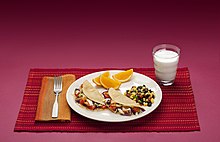 Dinner plate with fish tacos, oranges, corn, and beans, next to a cup of milk