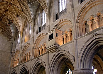 The Norman Malmesbury Abbey, showing the triforium, with its rounded arches and chevron mouldings, each arch supported by four small arches on columns. This triforium contains an unusual projecting watching-loft. There is also another passage above, at the base of the clerestory windows. Malmesbury, Wiltshire, England