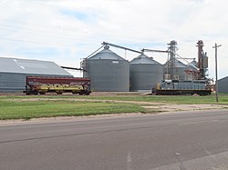 NKCR/Omnitrax diesel locomotive #414 (right) and a rail car (left) standing in front of grain silos at Imperial, NE, in June 2022