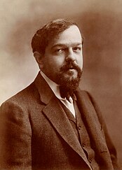 A man with a beard and moustache facing right wearing a black jacket and bow tie.