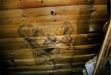 A wooden planked wall on which can be seen a stylised drawing of a woman's head and other ornamental shapes and objects