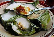Five banana leaves, filled with coconut milk and a sauce, on a plate