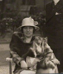 A finely-dressed woman in a white hat and fur coat
