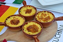 Four small clay pots covered with grated cheese, served on a table after baking