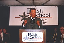 Former president George H.W. Bush speaks at a podium, emblazoned with the Bush School logo, with fists clenched in resolve.
