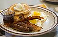 American style breakfast with pancakes, maple syrup, sausage links, bacon strips, and fried eggs