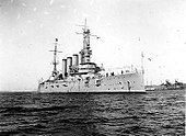 An armored cruiser anchored, with a navy jack flying from the jackstaff