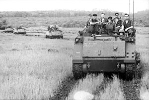 Black and white photo of three tracked military vehicles with men in military uniforms sitting on their roofs