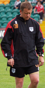 A man is looking down at the ground while walking, wearing a tracksuit top and shorts