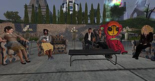 A screenshot of Second Life with people-like models sitting outside on couches around a coffee table. The person second from the right is in a red character suit. In the background in the distance, behind matchstick-shaped trees, are four towers. One tower is glowing with energy, and the tower on the far right is actually a giant space suit. Being a video game from the 2000s, the graphical fidelity is low, lacking shadows, ambient occlusion, and complex materials.