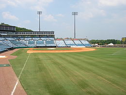 A view from the right field line of the seating bowl at Greer. Blue seats stretch from the right field wall, behind home plate, and beyond the third base dugout.