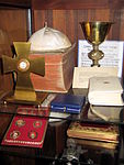Collection of items in the sacristy including white papal zucchetti, a chalice from the 15th century, rare Roman Missals, and 1st degree relics from various Roman Catholic saints