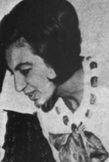 A young Afghan woman wearing a white top with a bow detail around the neckline; her dark hair is in a bouffant bob style