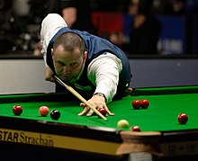 Stephen Maguire holds his cue and lines up a shot into a corner pocket.
