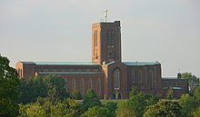 tall and long red brick cathedral with green roofs and square tower topped with gold angel