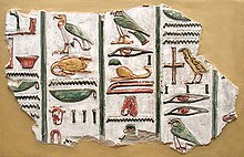 A stone fragment with brightly painted colors and raised-relief images of Egyptian hieroglyphs, written in vertical columns, set against a beige background
